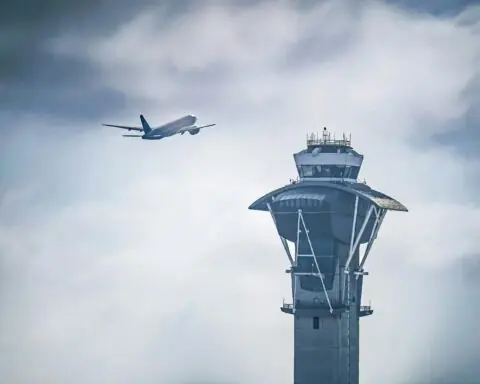 An air traffic control tower before a flying plane and cloudy blue sky in Los Angeles.
