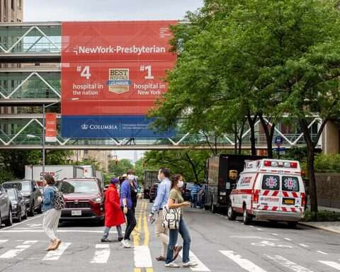 A busy street before an ambulance and a hospital skybridge.