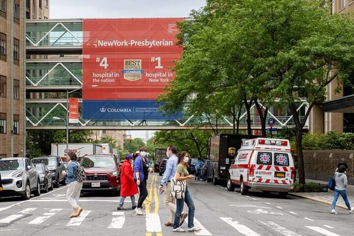 A busy street before an ambulance and a hospital skybridge.