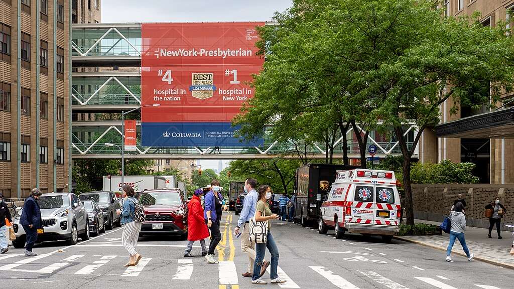 A busy street before an ambulance and a hospital skybridge.