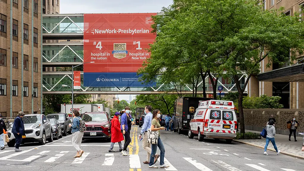 A busy street before an ambulance and a hospital skybridge.
