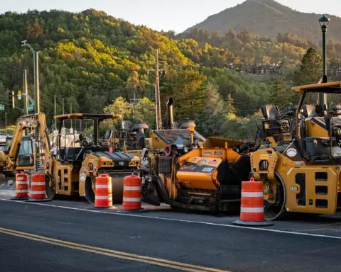 A lineup of construction vehicles alongside a road.