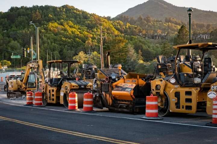 A lineup of construction vehicles alongside a road.