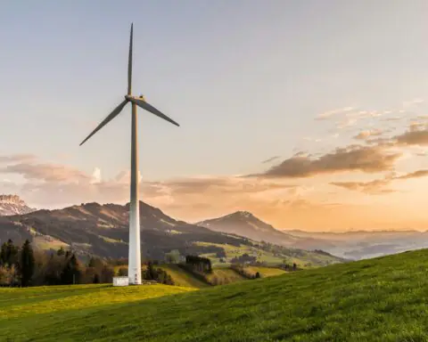 A white windmill before a setting sun and rolling hills.