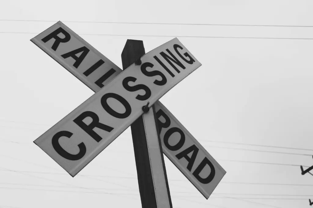 A black and white railroad crossing sign before a grey sky.