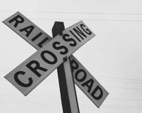 A black and white railroad crossing sign before a grey sky.