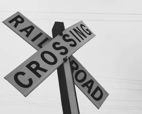 A black and white railroad crossing sign before a grey sky.