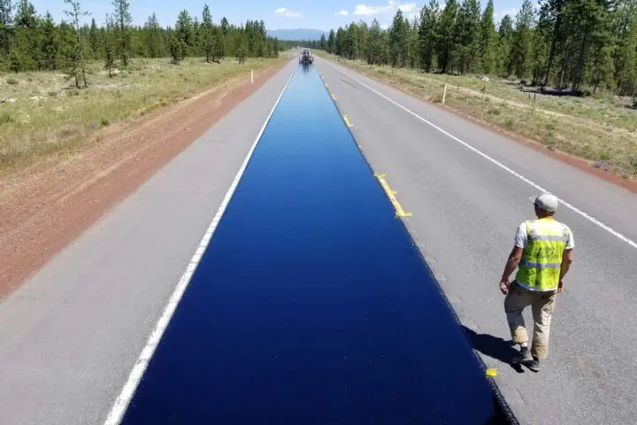 A newly repaved road next to a construction worker in a high-vis vest.