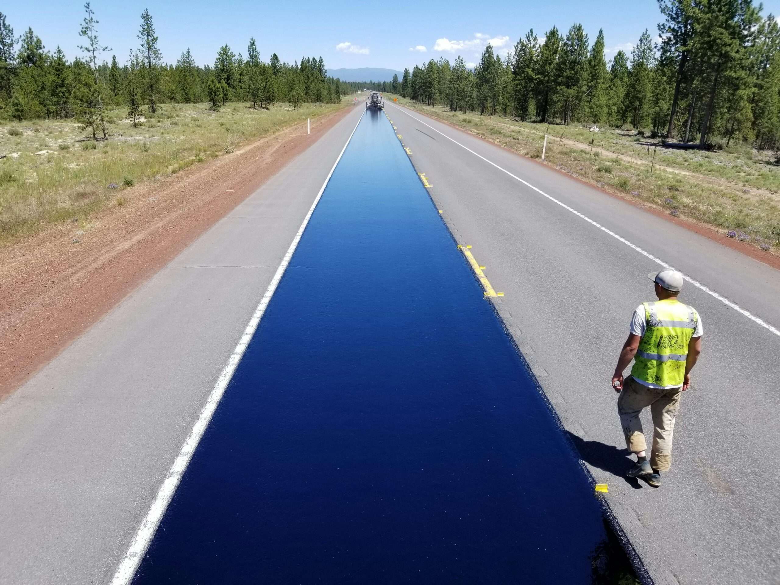 A newly repaved road next to a construction worker in a high-vis vest.