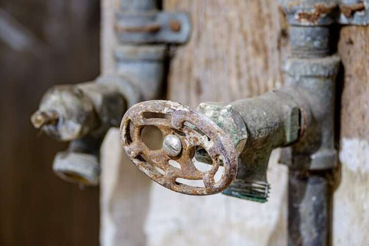 An old, rusty water tap outside in the sun.