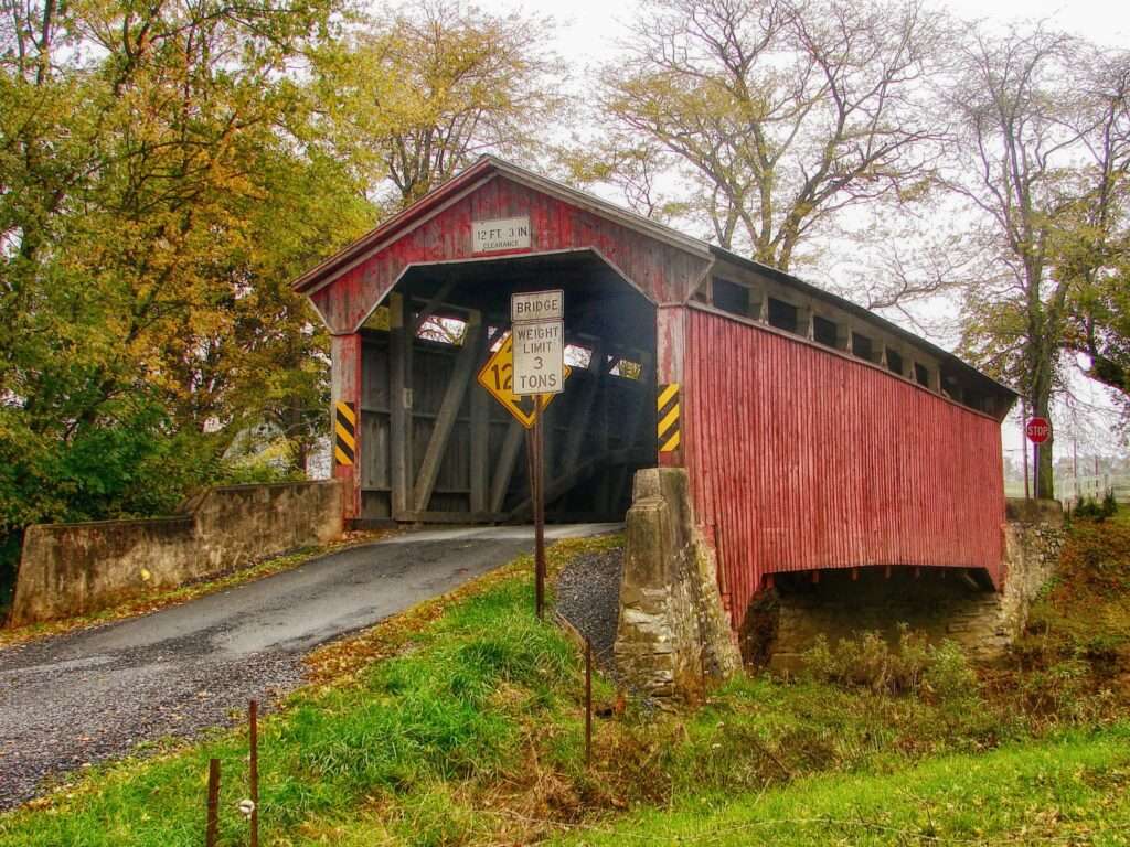 A covered wooden bridge in Pennsylvania on a cloudy day before Autumn trees.