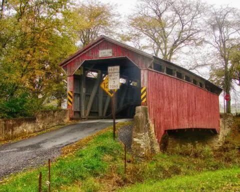 A covered wooden bridge in Pennsylvania on a cloudy day before Autumn trees.