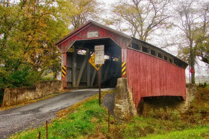 A covered wooden bridge in Pennsylvania on a cloudy day before Autumn trees.