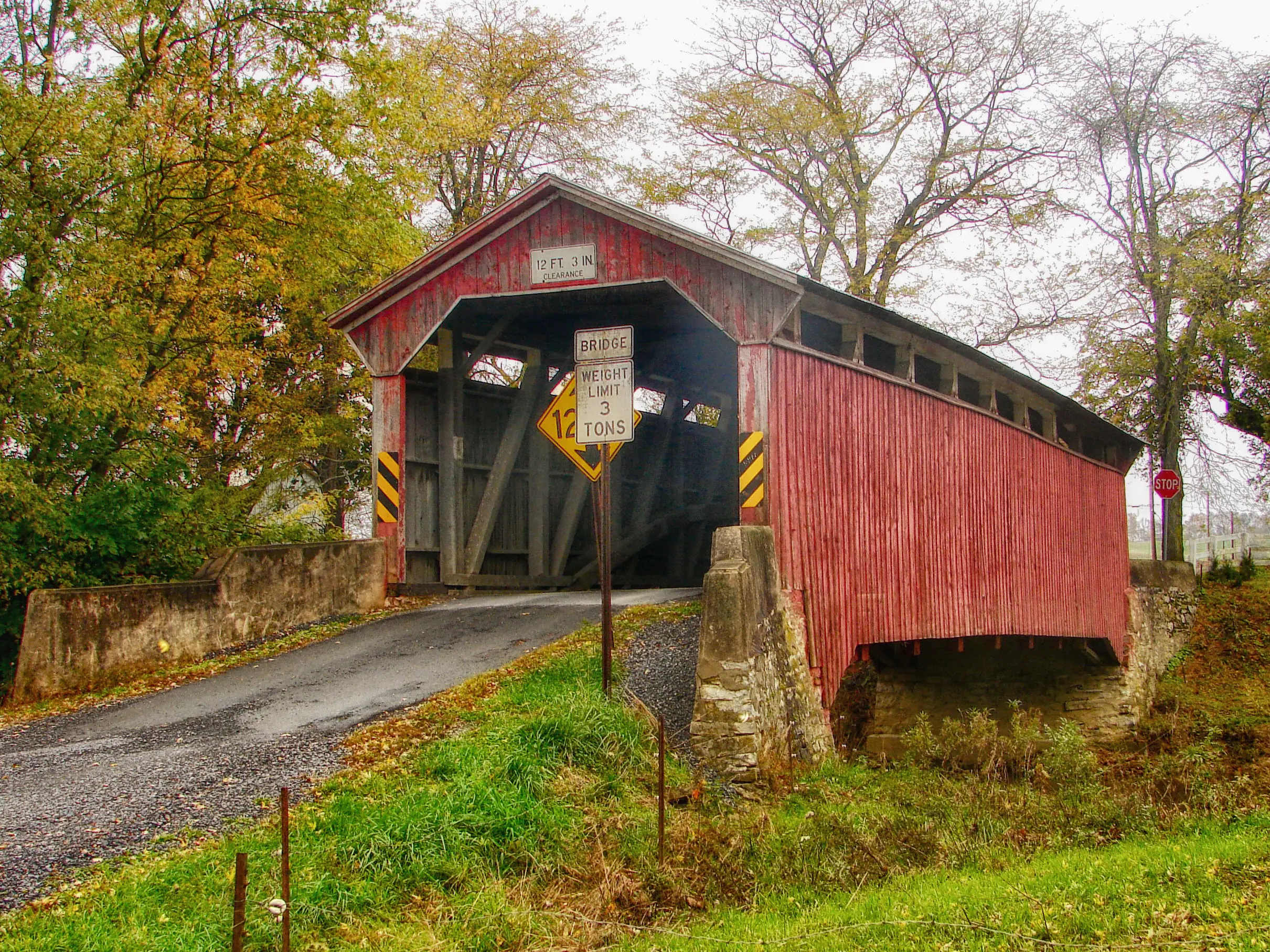 A covered wooden bridge in Pennsylvania on a cloudy day before Autumn trees.