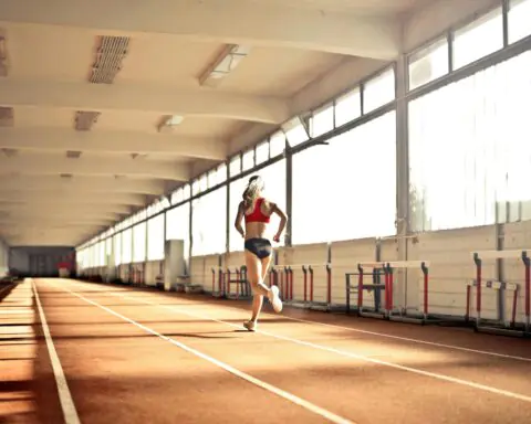 A woman runs alongside an indoor track at a fieldhouse.