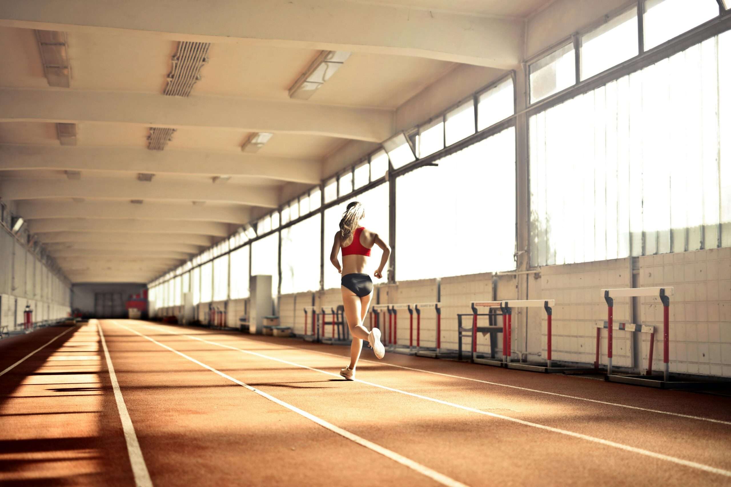 A woman runs alongside an indoor track at a fieldhouse.