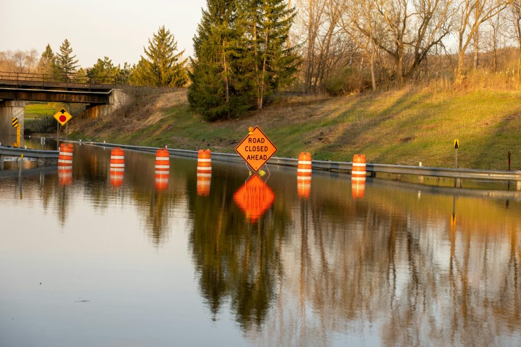 A flooded road with construction and road signs warning drivers.