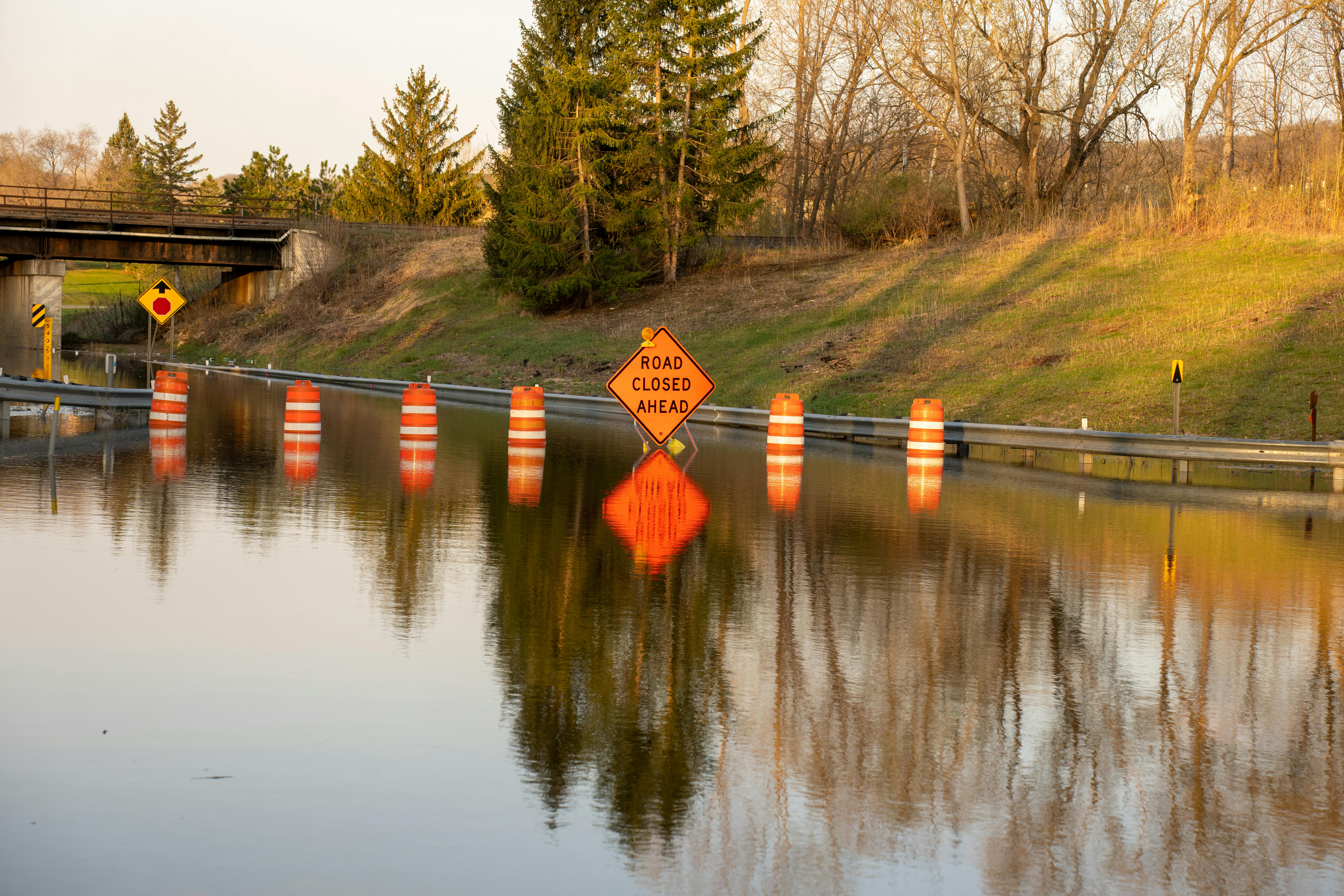 A flooded road with construction and road signs warning drivers.