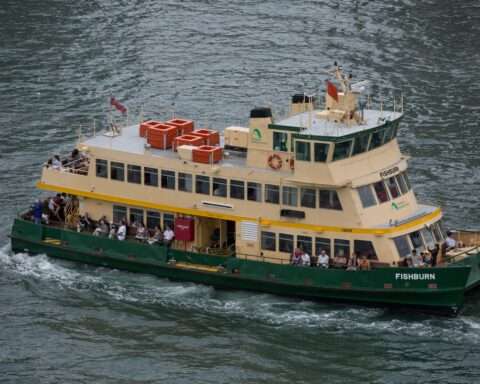 A ferry in the water with passengers before a deep blue body of water.