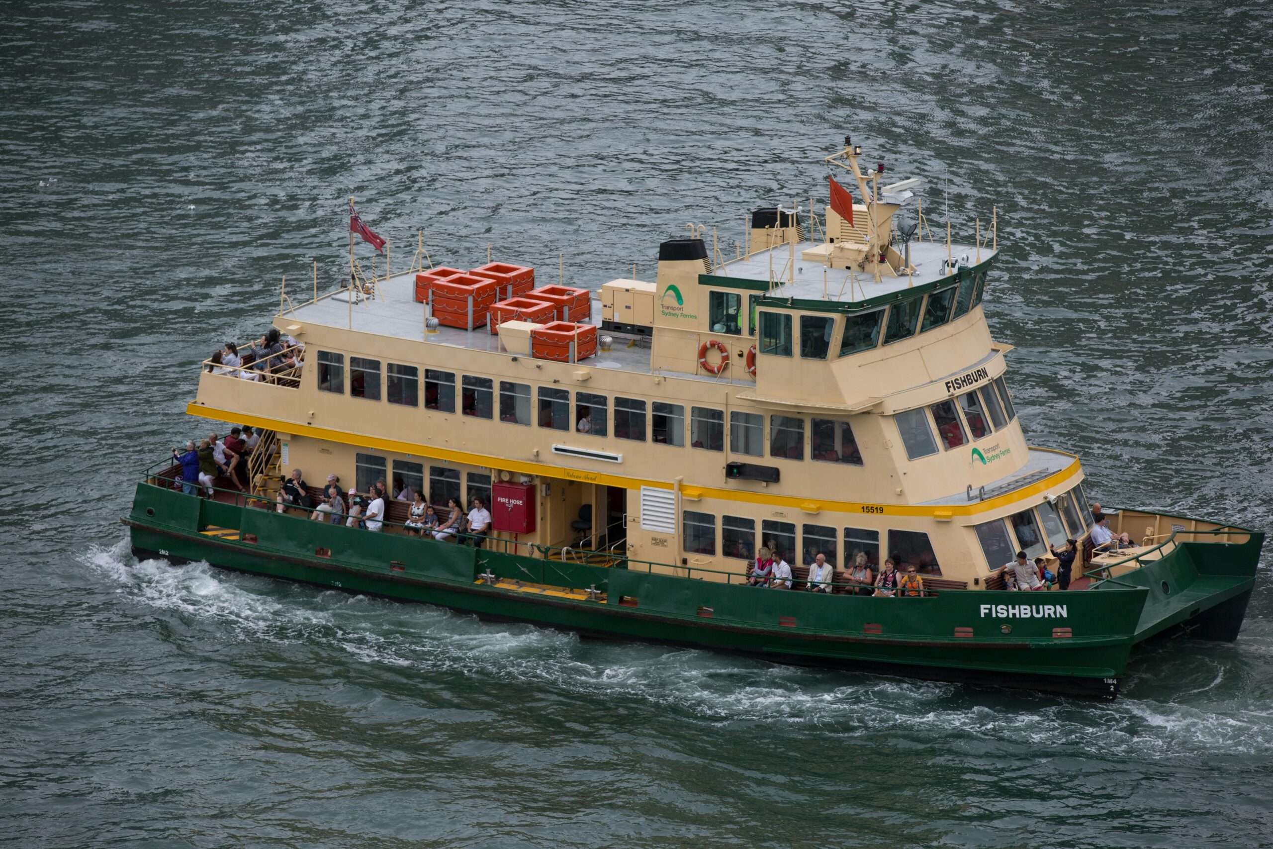 A ferry in the water with passengers before a deep blue body of water.