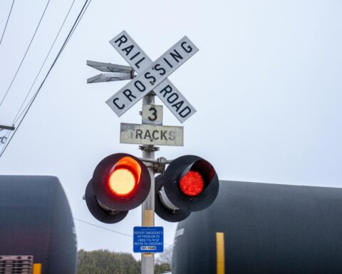 A rail crossing sign before a moving train carrying oil tankers.