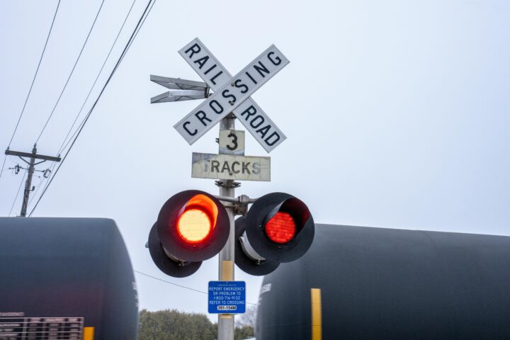 A rail crossing sign before a moving train carrying oil tankers.