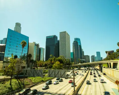 A highway full of cars in Los Angeles before city buildings on a sunny day.