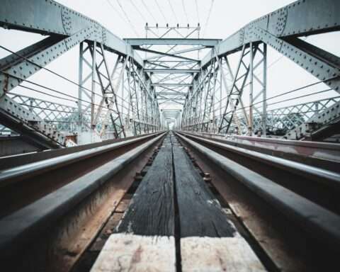 A ground up view of a rail-carrying bridge on a sunny day.