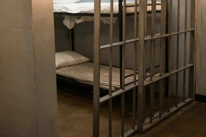 The interior of a jail cell with a bunk bed and two dumbbells.