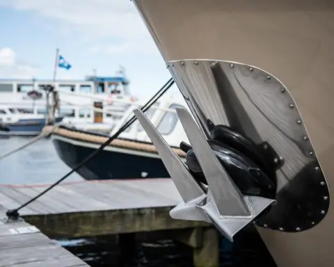 An anchored attached to a small ship at a shipyard on a sunny day before a second small vessel.