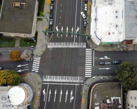 An aerial view of a roadway intersection with cars and pedestrians.