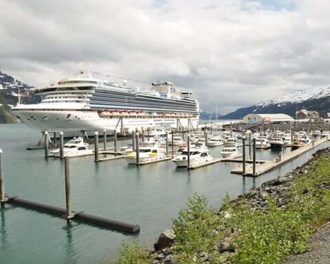 A cruise ship at port in Alaska near other ships and before a cloudy sky.