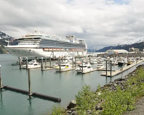 A cruise ship at port in Alaska near other ships and before a cloudy sky.