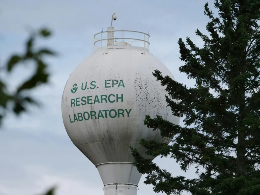 An EPA water tower behind the branches and leaves of several trees.