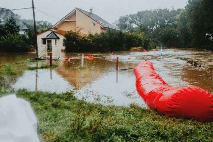 Flood mitigation strategies at work in a flooded street before a house and trees.
